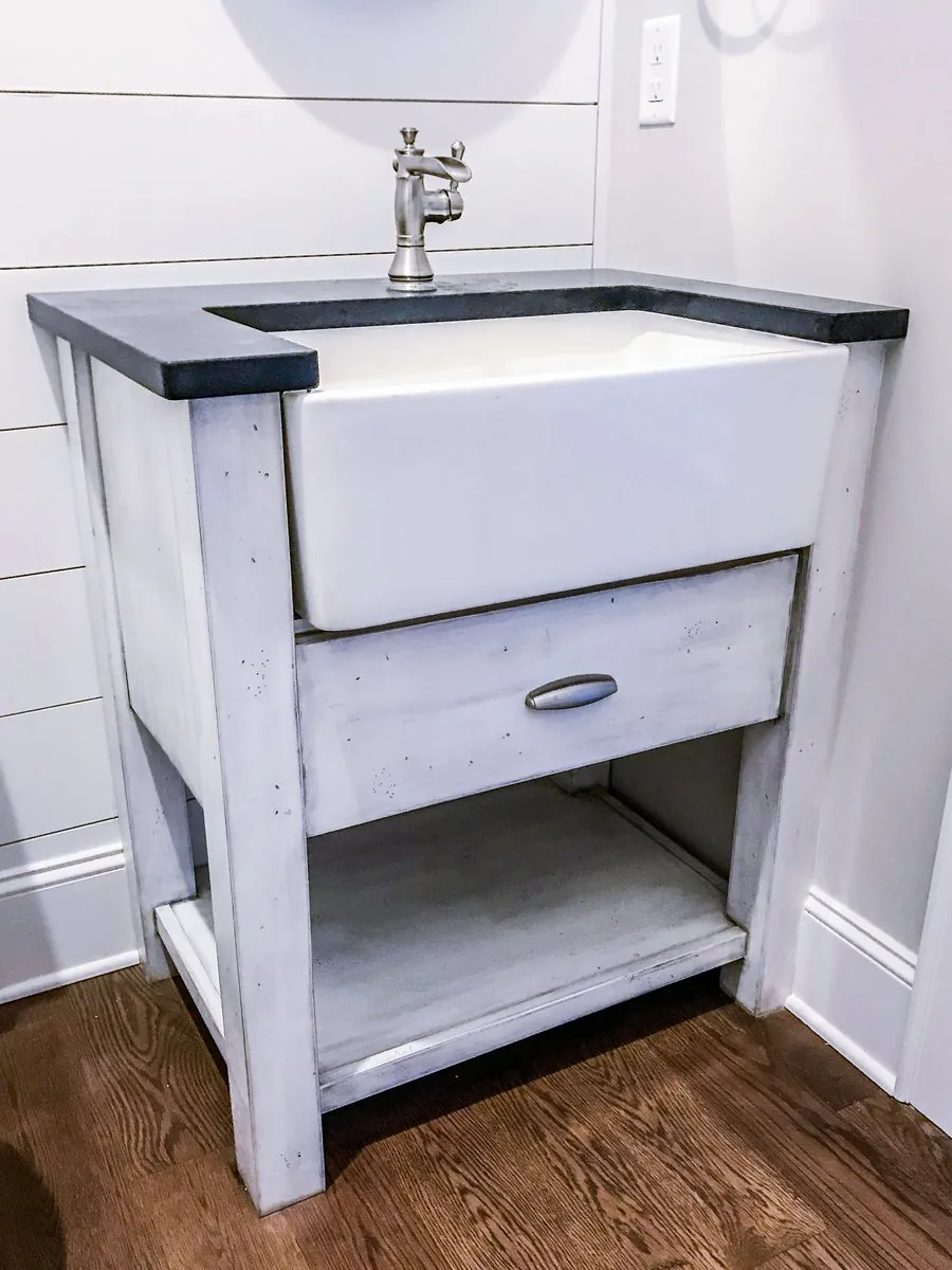 A freestanding vanity with an apron sink and an open lower shelf