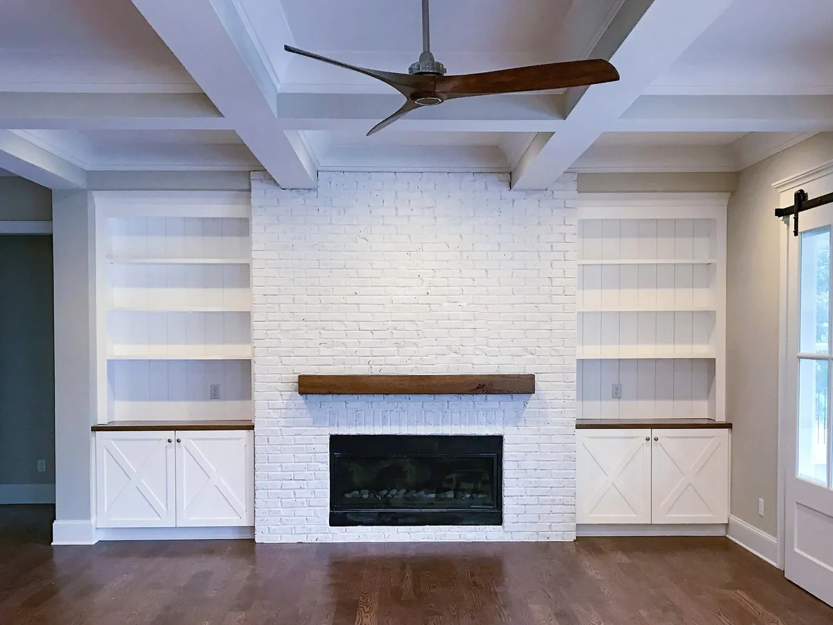 A painted brick fireplace with flanking built-in cabinets and shelves